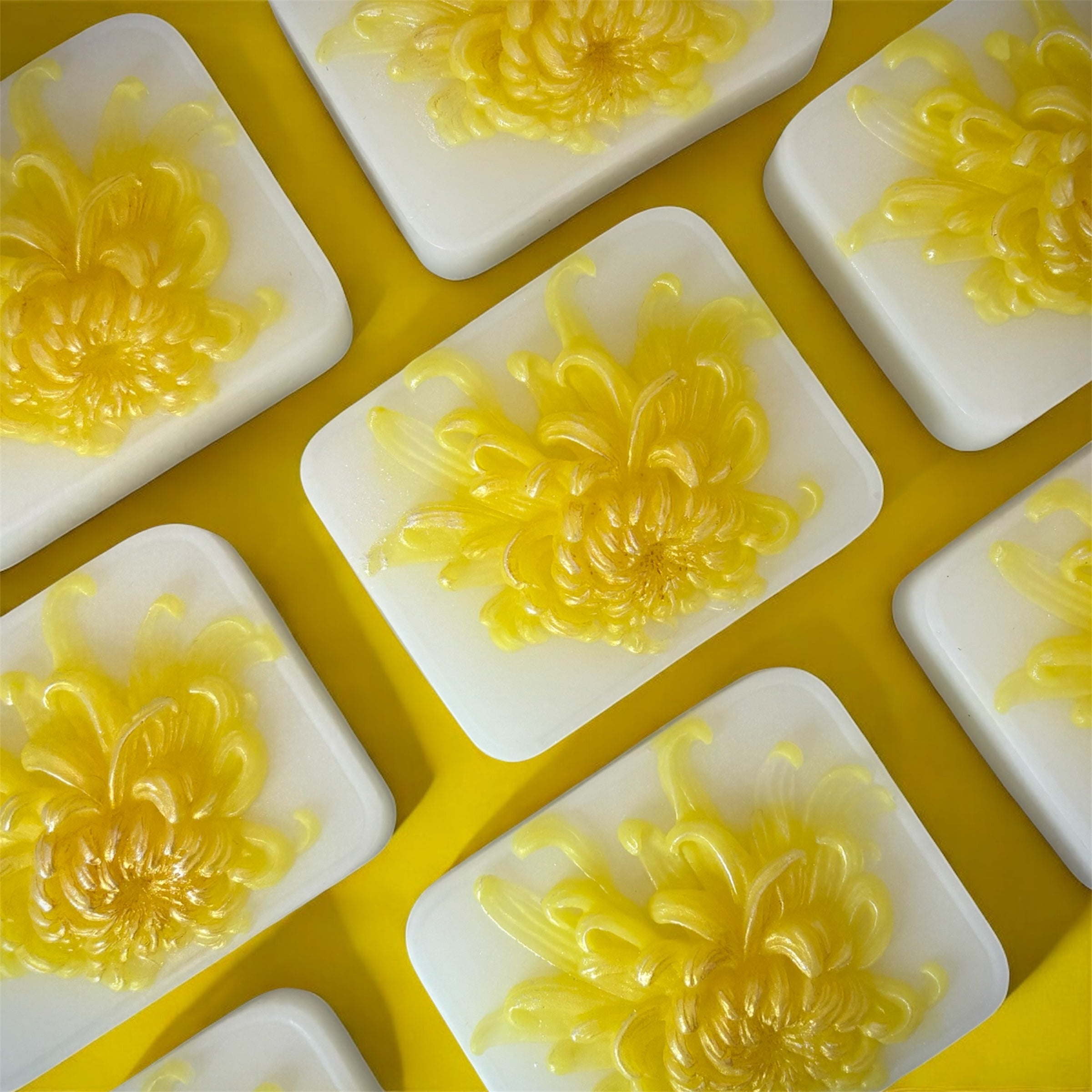 Yellow floral designs on white soap bars arranged in a grid on a yellow background